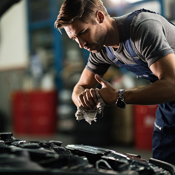Young auto mechanic cleaning hands after working on car engine in a garage
