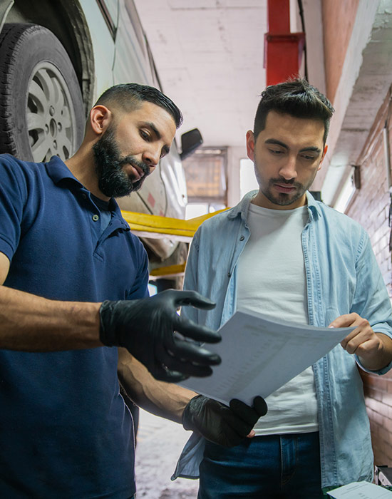 Male customer checking the list of the car parts changed at the auto repair shop with mechanic